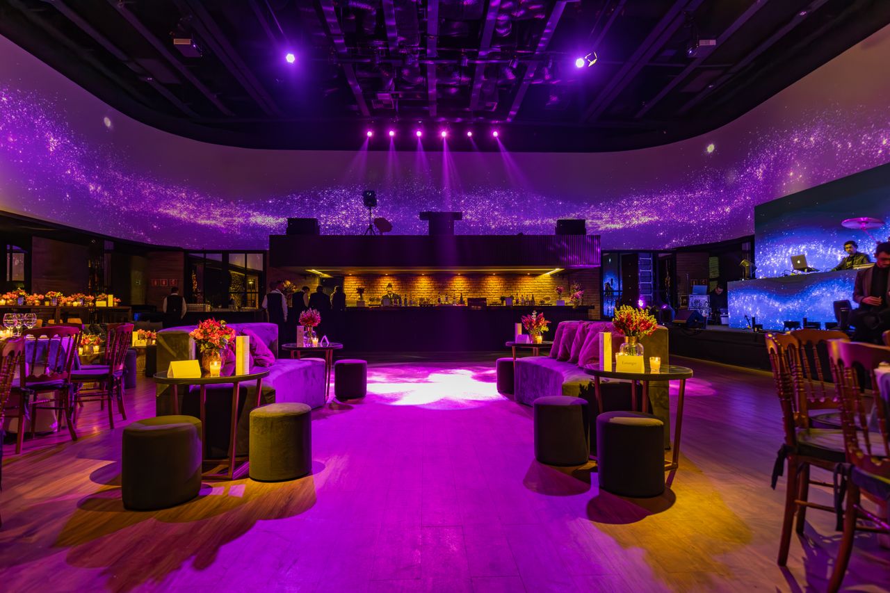 Elegant restaurant interior with purple lighting and stylish decor, featuring comfortable seating and floral arrangements.